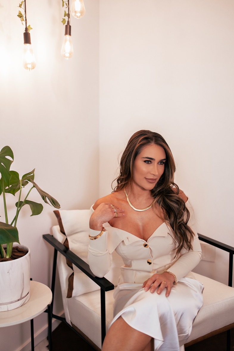 Mulher em produção editorial, sentada em ambiente iluminado com luz quente.