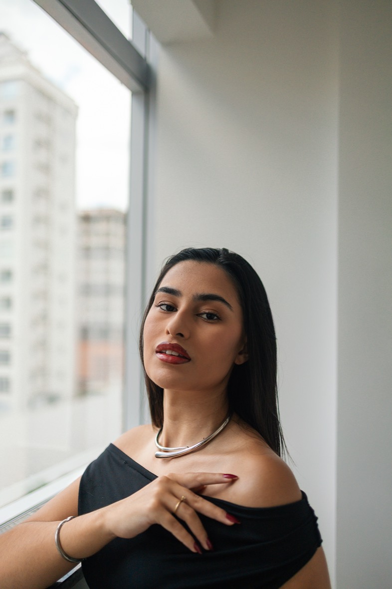 Registro do Patroa Day — retrato de beleza com colar prateado junto à janela.